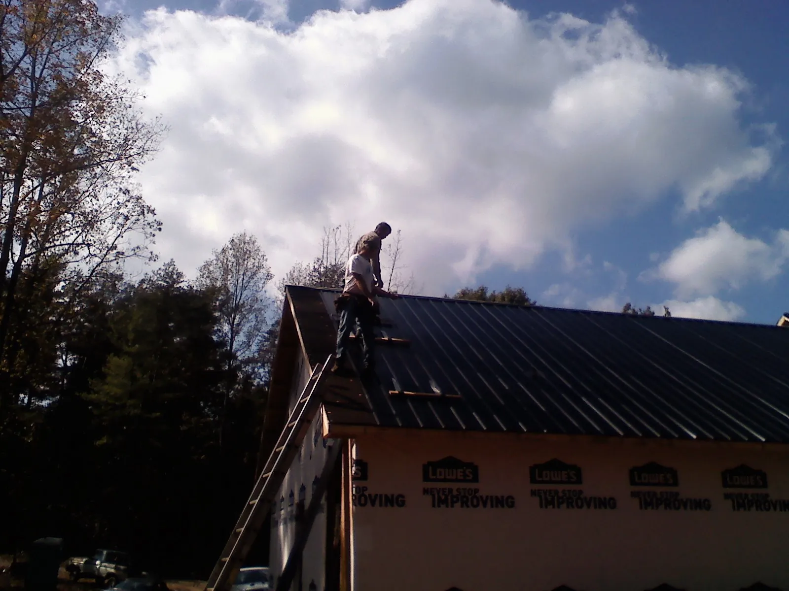 Roofer fastening dark metal panels high against a cloudy sky, from a Roof Inspection job in Luverne