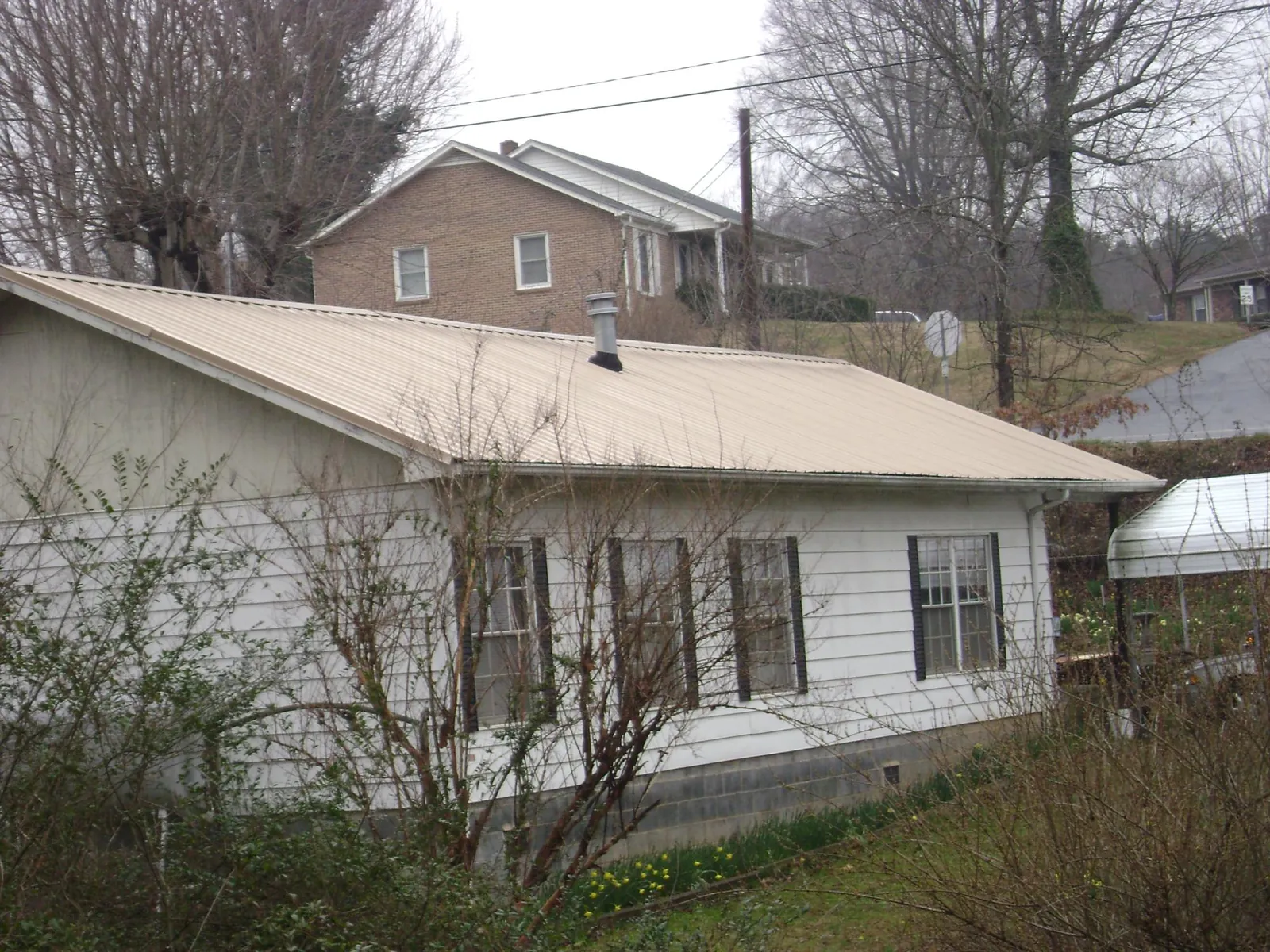 Tan metal roof on a white sided house set into a hillside — Commercial Roofing by Roofing Brothers in Luverne