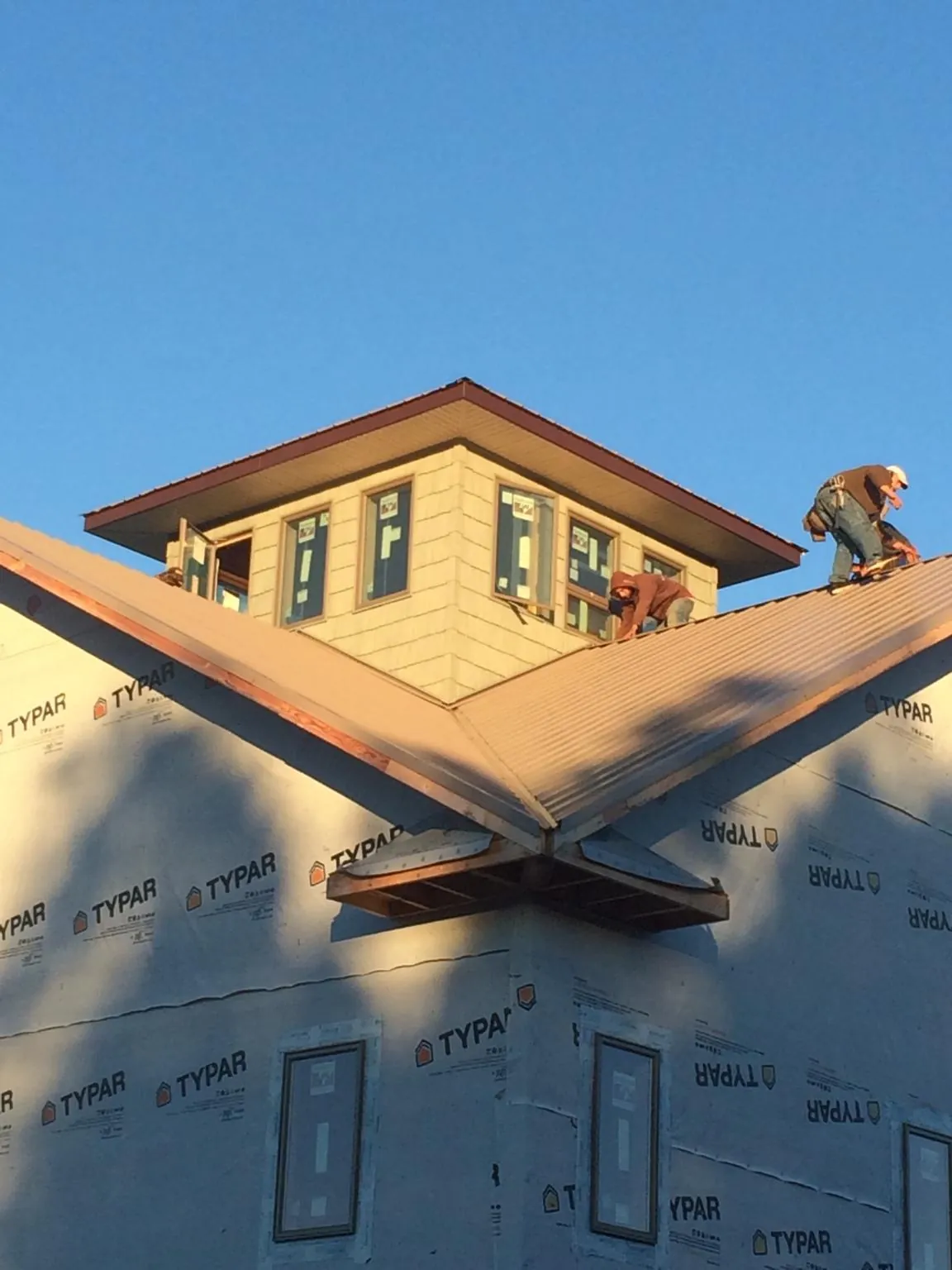 Roofers working around a rooftop cupola on a new metal roof at sunset — Roof Waterproofing in Luverne by Roofing Brothers